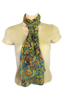 A lightweight scarf with a vibrant floral pattern in green, yellow, and orange, styled with a loose knot 