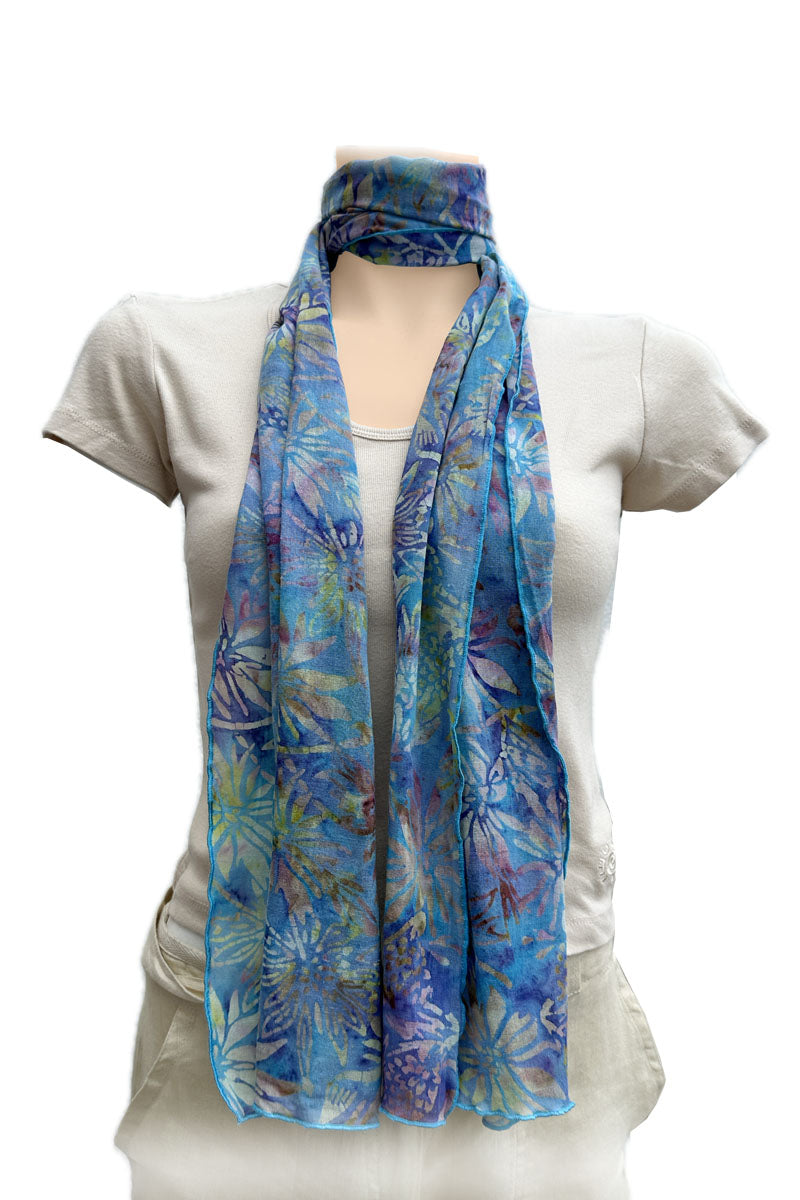 A lightweight blue scarf with a tropical floral print, styled at the nect with a loop.