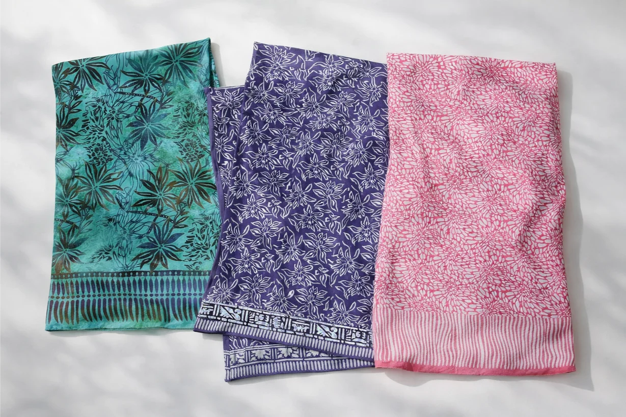 Three patterned scarves in green, purple, and pink on a light gray background