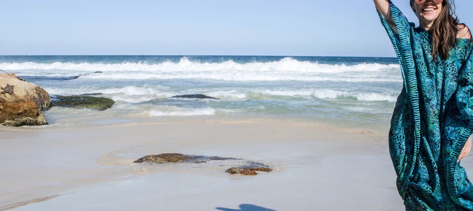 Person wearing a blue batik printed kaftan with floral pattern on a beach